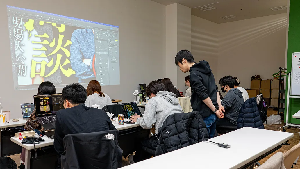 講師の指導を受けながらパソコンでデザイン制作に取り組む受講者